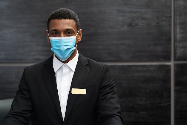 Recepcionista masculino en traje en el trabajo con máscara médica