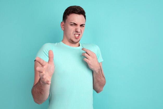 Rechazando, disgustado. Retrato de joven caucásico aislado en la pared azul. Hermoso modelo masculino de estilo casual, colores pastel. Concepto de emociones humanas, expresión facial.