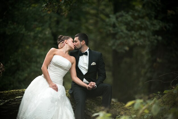 Recién casados besándose con un bosque de fondo