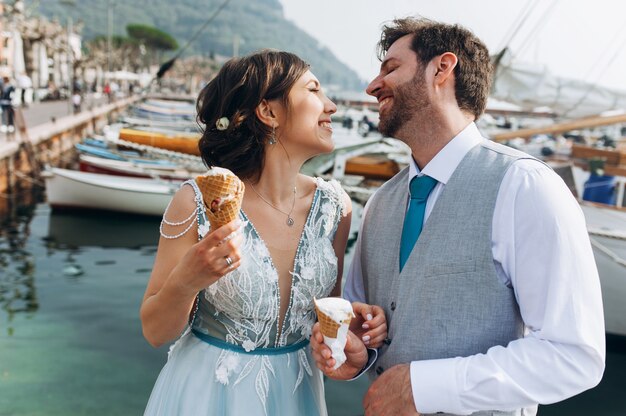 Los recién casados ​​divertidos comen el helado que se coloca antes de los barcos