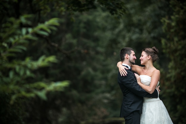 Recién casados mirandose a los ojos con un bosque de fondo