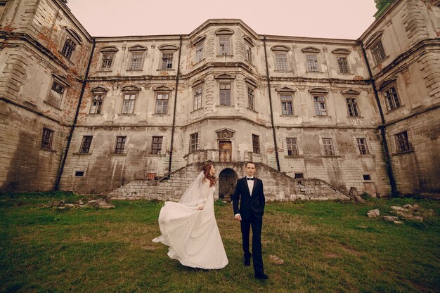 Recién casados sonrientes con castillo antiguo de fondo