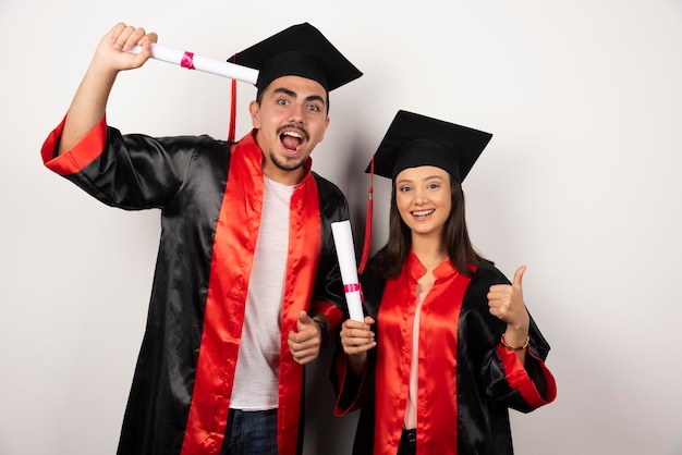 Recién graduados con diploma haciendo pulgares hacia arriba en blanco.