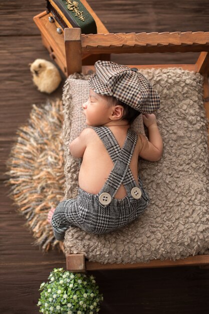 Recién nacido pequeño bebé bonito niño acostado en la cama de madera en traje de bebé y sombrero