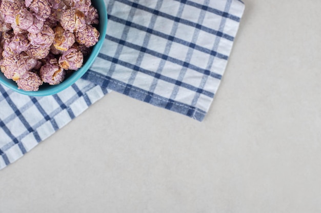 Foto gratuita recipiente azul descansando sobre una toalla doblada y lleno de palomitas de maíz recubiertas de caramelo sobre una mesa de mármol.