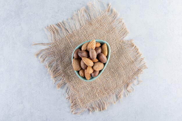 Recipiente azul lleno de almendras y nueces sin cáscara sobre fondo de piedra.