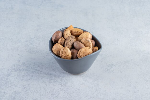 Recipiente azul lleno de almendras y nueces sin cáscara sobre fondo de piedra.