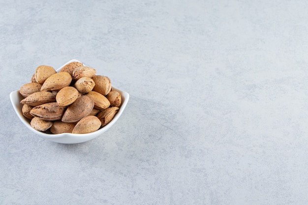 Recipiente blanco lleno de almendras sin cáscara sobre fondo de piedra.