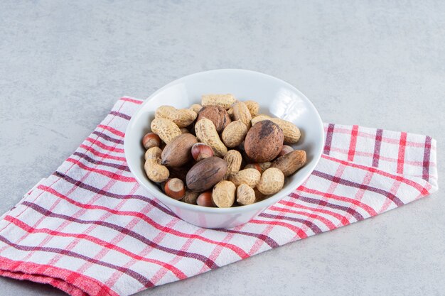 Recipiente blanco lleno de diversas nueces sin cáscara sobre fondo de piedra.