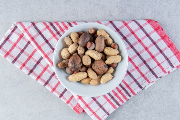 Recipiente blanco lleno de diversas nueces sin cáscara sobre fondo de piedra.