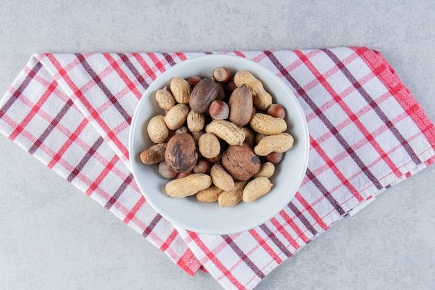 Recipiente blanco lleno de diversas nueces sin cáscara sobre fondo de piedra.