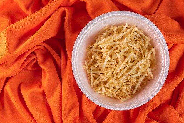 Recipiente blanco con paja de patata sobre fondo naranja