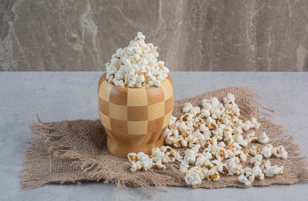 Recipiente a cuadros lleno de palomitas de maíz sobre un trozo de tela con un puñado de palomitas de maíz sobre la superficie de mármol