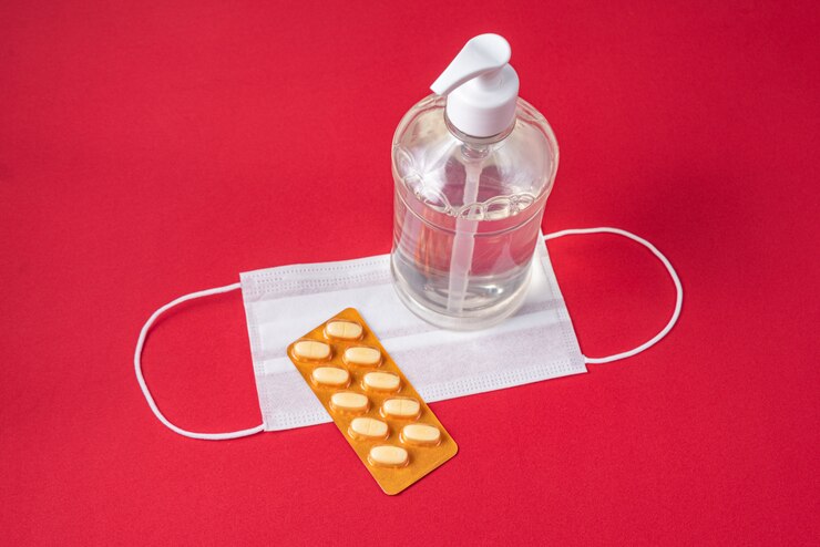 Foto gratuito recipiente de gel de alcohol, mascarilla quirúrgica, medicamento en la pared roja