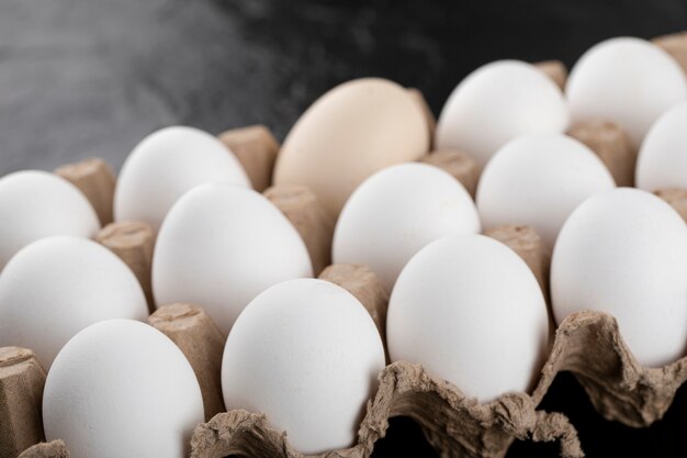 Recipiente de huevos blancos sobre superficie negra.