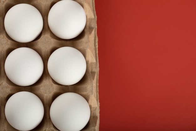 Recipiente de huevos blancos sobre superficie roja.