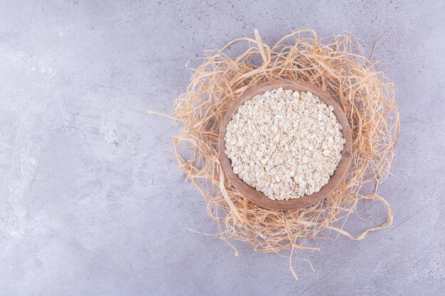 Recipiente lleno de avena crujiente colocada sobre un montón de pajitas de fondo de mármol. Foto de alta calidad