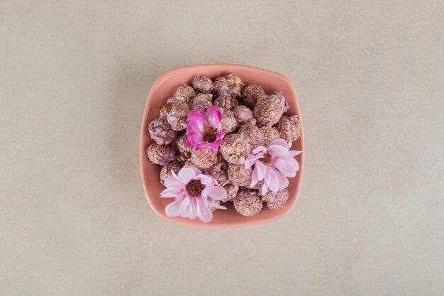 Recipiente lleno de palomitas de maíz recubiertas de caramelo con flores sobre mármol.