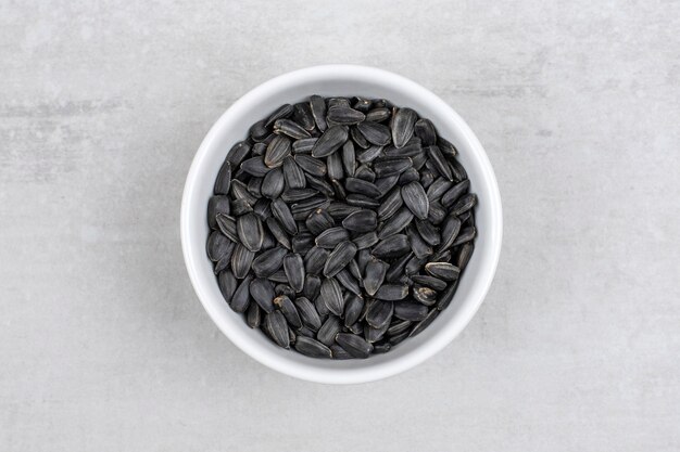 Recipiente lleno de semillas de girasol negras colocadas sobre la mesa de piedra.