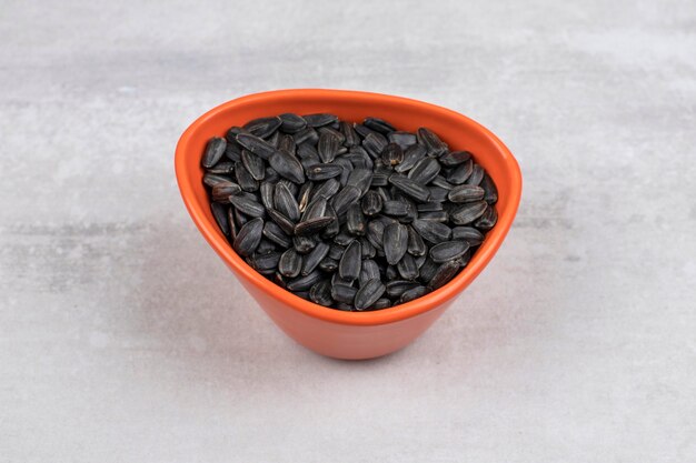 Recipiente lleno de semillas de girasol negras colocadas sobre la mesa de piedra.