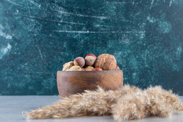 Recipiente de madera lleno de diversas nueces sin cáscara sobre fondo de piedra.