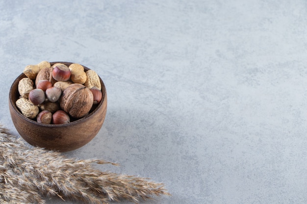 Recipiente de madera lleno de diversas nueces sin cáscara sobre fondo de piedra.