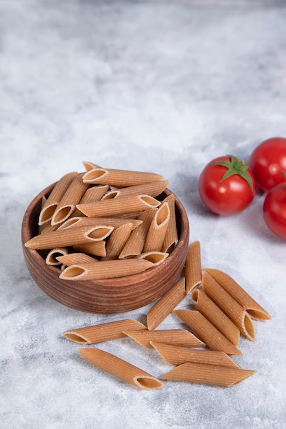 Recipiente de madera lleno de pasta cruda integral penne colocado sobre una mesa de mármol. Foto de alta calidad