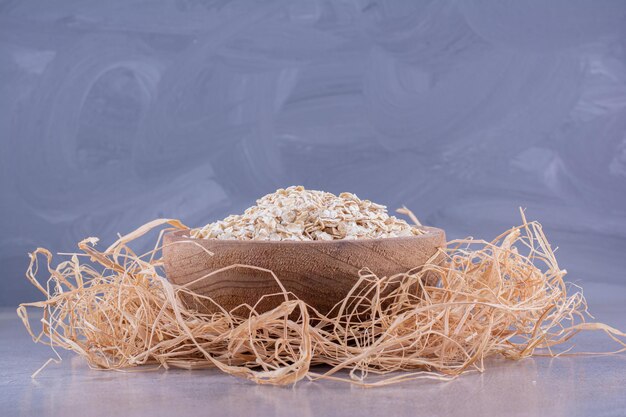 Recipiente pequeño lleno de avena colocado encima del montón de paja decorativa sobre fondo de mármol. Foto de alta calidad