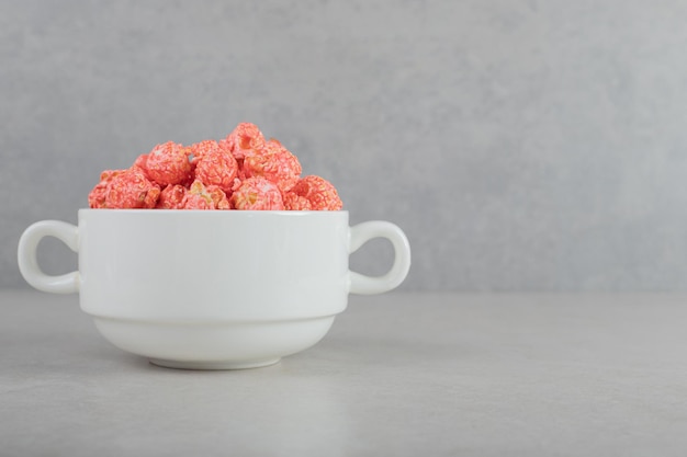 Recipiente pequeño lleno de palomitas de maíz recubiertas de rojo sobre fondo de mármol.