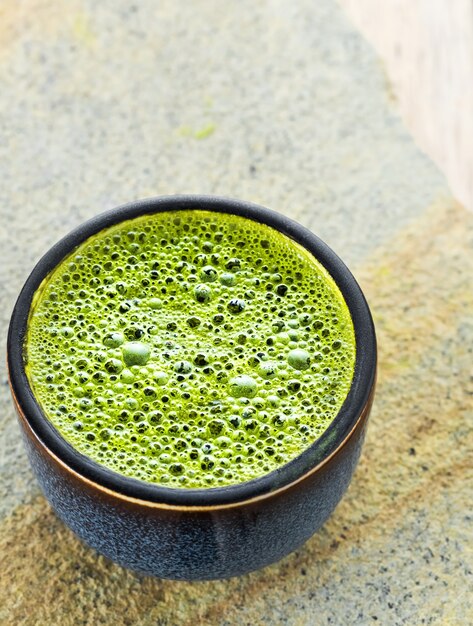 Recipiente con té verde matcha con espuma sobre una superficie de piedra gris