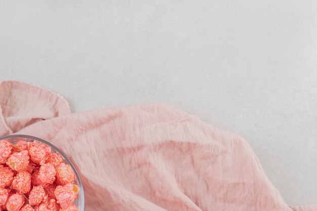 Recipiente de vidrio de caramelo de palomitas de maíz descansando sobre un trozo de tela rosa sobre una mesa de mármol.