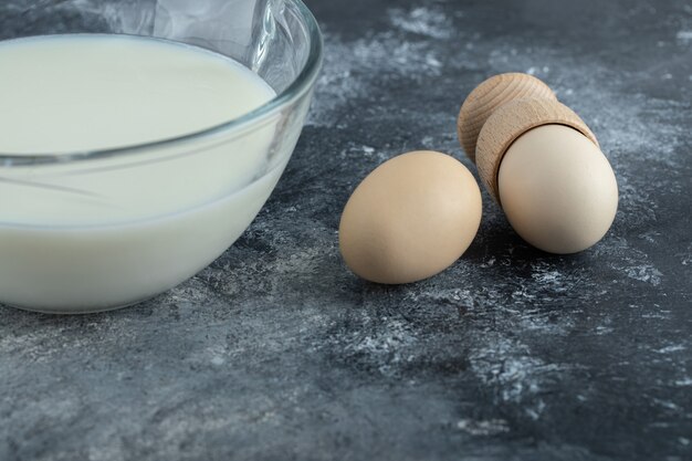 Recipiente de vidrio lleno de leche fresca y huevos en mármol.