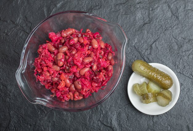 Recipiente de vidrio de repollo en escabeche con frijoles rojos y pepinos sobre fondo negro