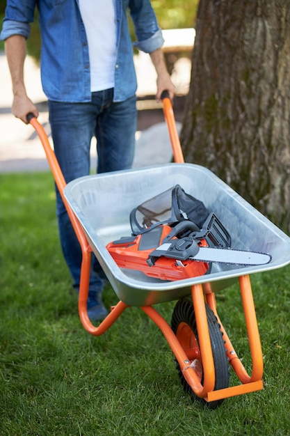 Foto gratuita reconocible jardinero masculino fuerte empujando carrito para el transporte de equipos de metal de cerca