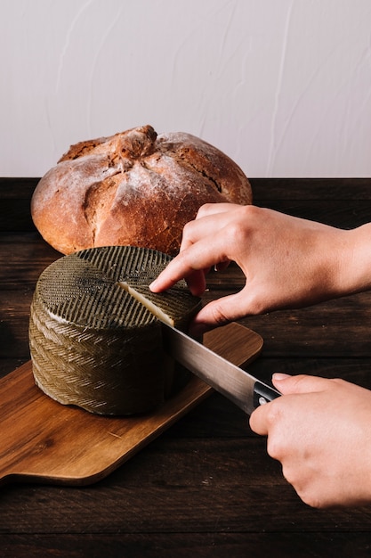 Foto gratuita recortar las manos cortando queso cerca del pan