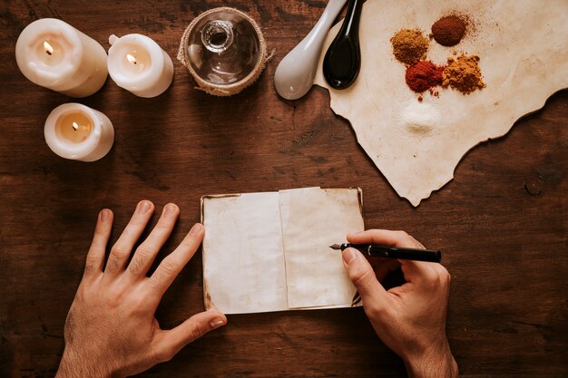 Recortar manos escribiendo cerca de velas e ingredientes