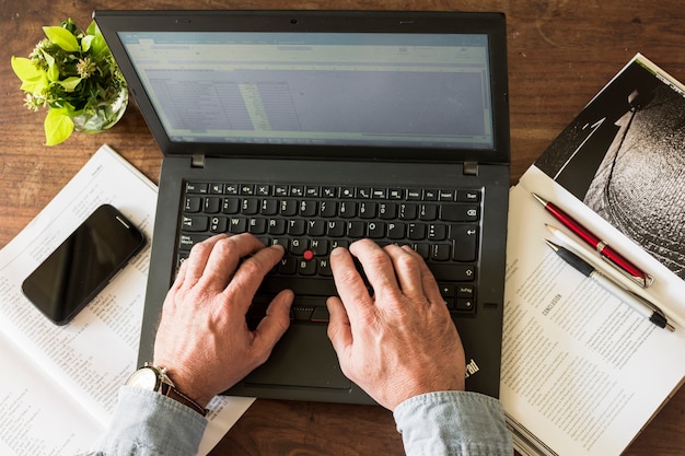 Foto gratuita recortar las manos escribiendo en la computadora portátil en la oficina