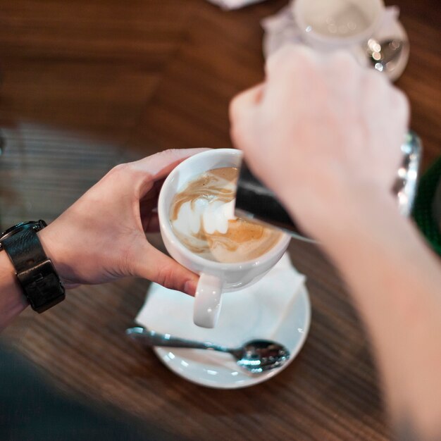 Recortar las manos haciendo espuma en el café con leche