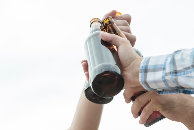 Recortar las manos de los hombres que tintinean botellas de cerveza