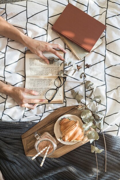 Recortar las manos con el libro cerca de alimentos para el desayuno y ramitas