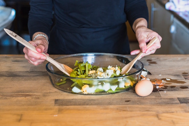 Recortar las manos de mujer cocinando ensalada sabrosa en la cocina