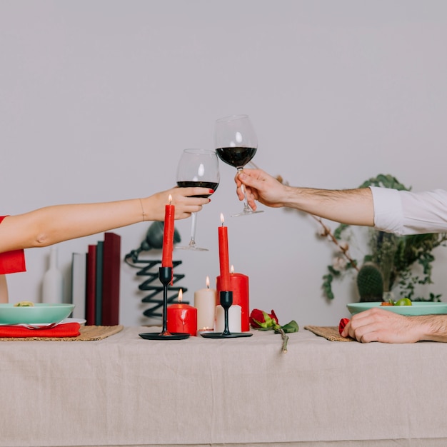 Recortar las manos tintineando vasos durante la cena romántica