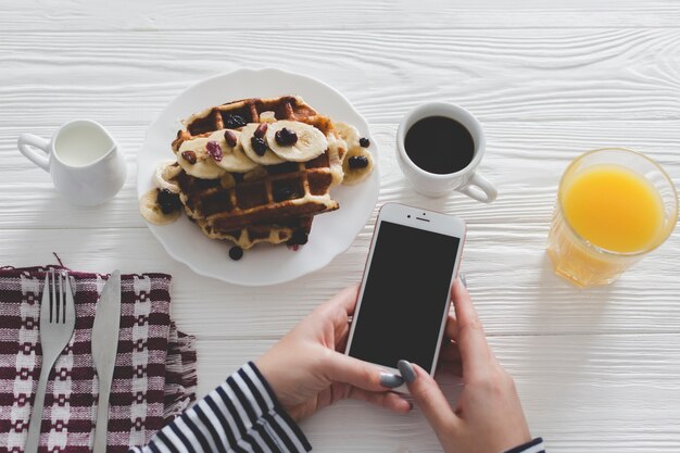 Recortar las manos usando el teléfono inteligente durante el desayuno