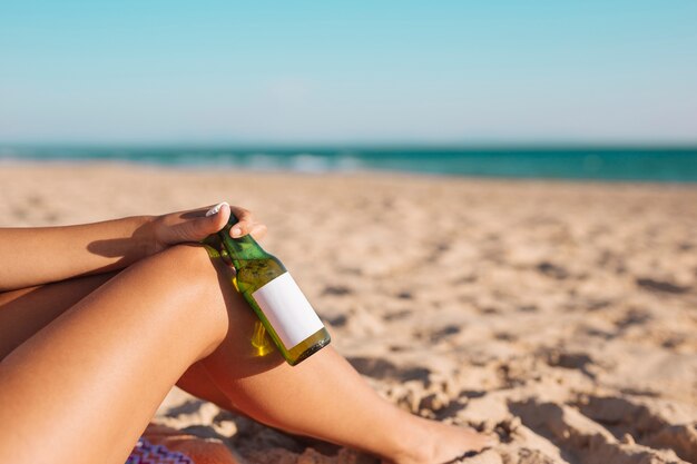 Recortar piernas femeninas y mano con cerveza.