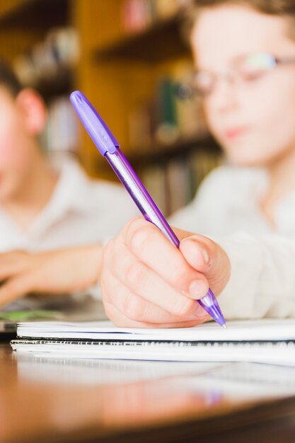 Recorte de la mano del niño escribiendo en el cuaderno de la escuela