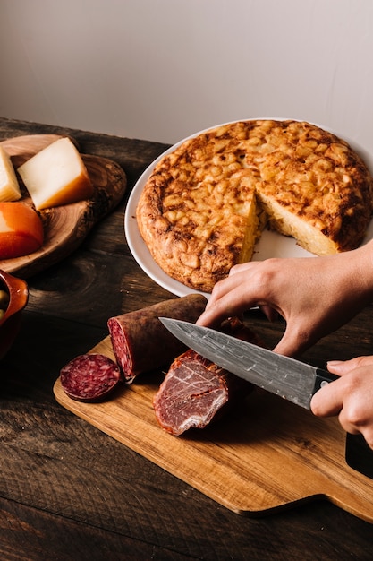 Foto gratuita recorte las manos cortando salchicha cerca de la tarta