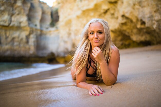 Recreación de verano y concepto de viajes. Hermosa modelo de moda joven bronceada en bikini posando en la costa del mar. Mujer en traje de baño de playa con el pelo mojado y el cuerpo acostado en una playa
