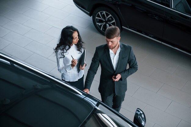 Recuerda qué decir en la reunión. Clienta y empresario barbudo con estilo moderno en el salón del automóvil