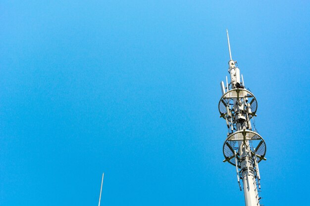 Red y blanco torre de comunicaciones con un montón de diferentes antenas bajo el cielo azul y las nubes