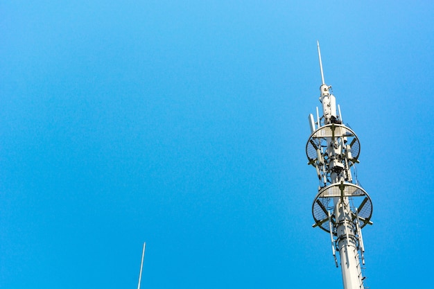 Red y blanco torre de comunicaciones con un montón de diferentes antenas bajo el cielo azul y las nubes